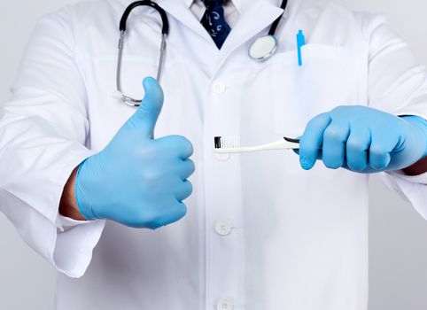 adult doctor therapist is dressed in a white robe uniform and blue sterile gloves is standing and holding a toothbrush, daily brushing concept, white background