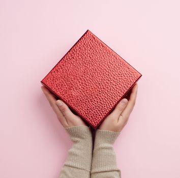 female hand holds a red box, concept of congratulations and gifts, top view, pink background