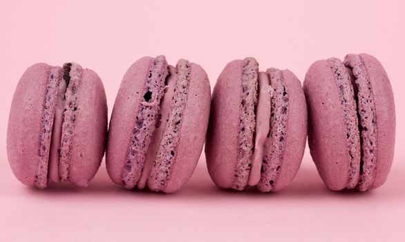 four round purple almond flour dessert macarons with cream on a pink background, delicious cake, close up