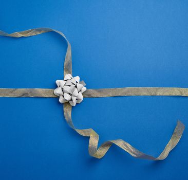 golden ribbon crossed on a dark blue background in the middle of a gray bow, imitation of tying a gift, top view