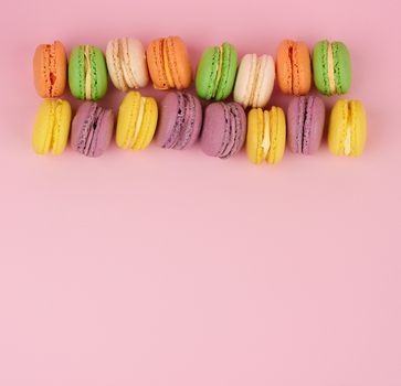 yellow, purple round baked macarons cakes on a pink background, dessert lies in a row, top view, copy space