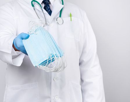 doctor in a white coat, blue latex sterile gloves holds textile medical masks in his hand, protective accessory against viruses and bacteria, close up
