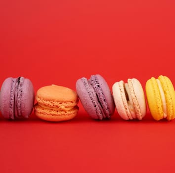 yellow, purple, green round baked macarons cakes on a red background, dessert lies in a row, close up
