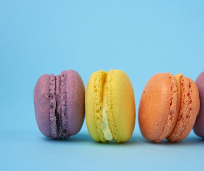 multi-colored round baked macarons cakes on a light blue background, dessert stands in a row, close up