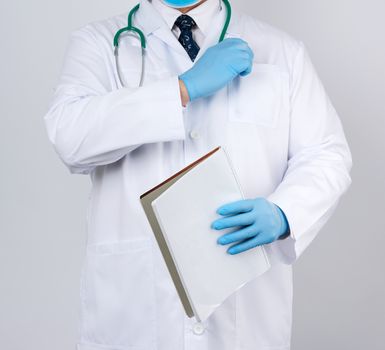 male doctor in a white coat with buttons, wearing blue sterile gloves, holding a paper notebook in his hand on a white studio background