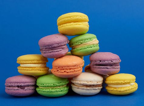 stack of multi-colored round baked macarons cakes on a dark blue background, close up