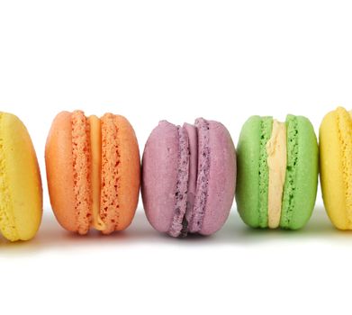 multi-colored round baked macarons cakes on a white isolated background, dessert stands in a row, close up