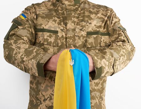 Ukrainian man warrior dressed in a military pixel uniform holds the yellow-blue flag of the state of Ukraine and on the chain a small coat of arms of the country of trident, white background 
