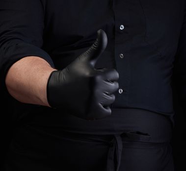 male cook in black uniform and black latex gloves shows like approval gesture, close up