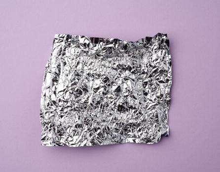 crumpled foil used candy wrappers on a lilac background, top view