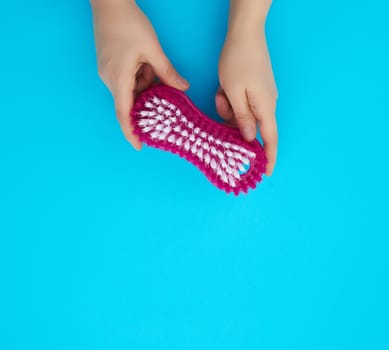 hand holds a plastic brush for cleaning housework, blue background, close up