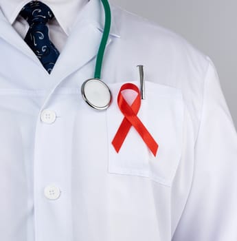 doctor in a white coat and tie is standing on a white background, red silk ribbon is hanging on his chest, symbol of the fight against disease AID