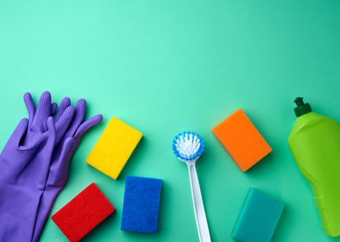 purple rubber gloves for cleaning, multi-colored sponges, brushes and cleaning fluid in a green plastic bottle on a green background, place for text, flat lay
