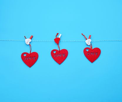 three red felt hearts hanging on a white rope and fastened with a clothespin, blue background. Holiday celebration concept. 