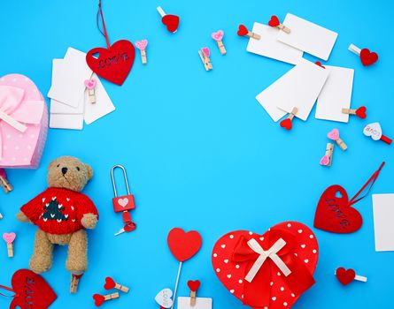 cardboard boxes in the form of a heart, a small teddy bear, white blank business cards with clothespins on a blue background, decor and objects for Valentine's Day, flat lay, copy space