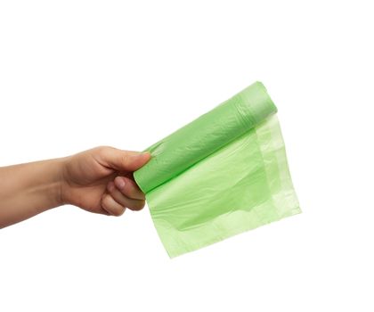 female hand holds a bundle of green plastic bags for garbage, part of the body with the subject isolated on a white background