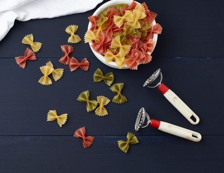 raw pasta in the form of bows in a wooden round plate and white textile napkin on a blue wooden background, top view. Vegetarian nutrition. Italian cuisine