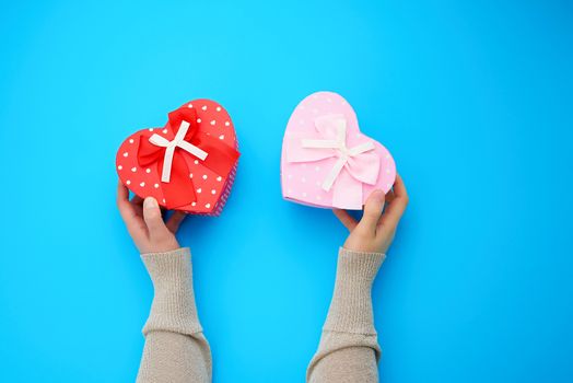 two female hands holding a red and pink cardboard box in the shape of a heart on a blue background, top view