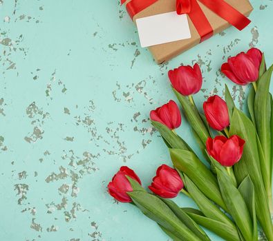 bouquet of red blooming tulips with green leaves, wrapped gift in brown craft paper on a green background, copy space. Festive backdrop for birthday, Valentine's day