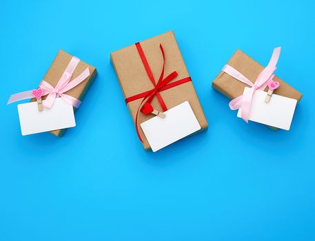 box is wrapped in brown paper and tied with a red thin silk ribbon on a blue background, copy space, holiday is Valentine's Day