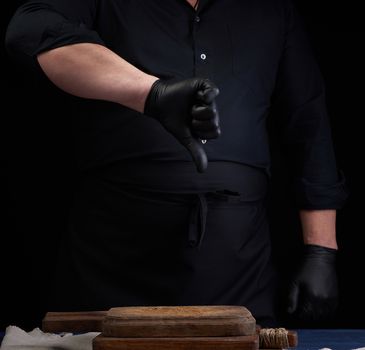 chef in black latex gloves and a black uniform shows with his right hand a gesture of dislike, low key
