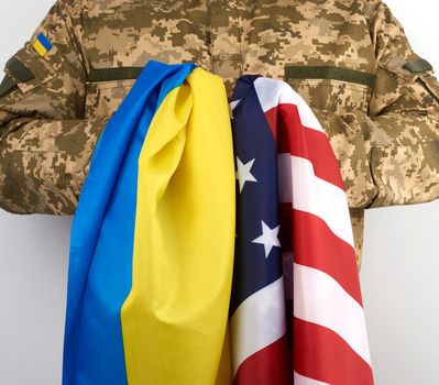 Ukrainian army soldier holds the flags of Ukraine and the United States in his hands, concept of friendship, partnership