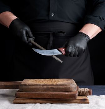 chef in a black shirt and black latex gloves sharpen a kitchen knife on an iron sharpener with a handle above the table, low key