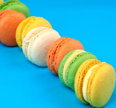 round multi-colored baked macarons with cream lie in a line on a blue background, close up