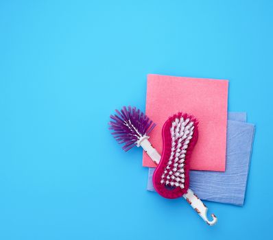 plastic pink brush and square dishwashing rag on a blue background, top view, flat lay