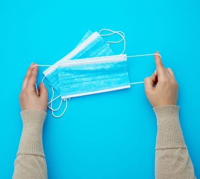 female hands protracted blue sterile textile medical mask with white elastic bands for doctors on a light blue background, flat lay