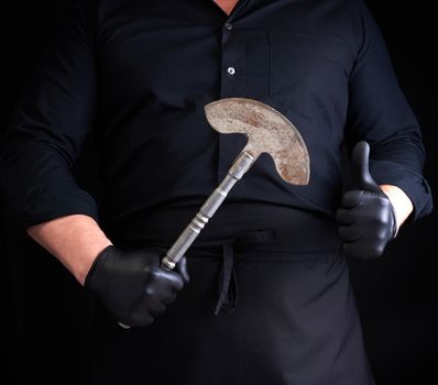 man in black clothes, latex gloves holds a vintage metal ax-knife for meat and vegetables, dark background