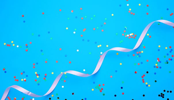 shiny multicolored round confetti scattered on a blue background and pink ribbon, festive backdrop for birthday, valentines day
