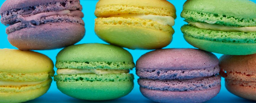 multi-colored round baked macarons cakes on a  blue background, banner 