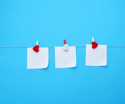 three empty square white paper sheets hanging on decorative clothespins, blue background