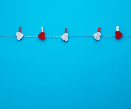 wooden decorative clothespins with carved felt hearts hang on a rope, blue background
