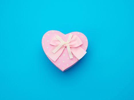 pink gift box in the form of a heart with a bow on a blue background, top view, festive backdrop