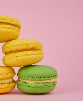 stack of yellow and green round almond flour cakes macarons with cream on a pink background, delicious cake