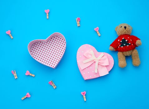 open empty cardboard box in the form of a heart and little brown teddy bear on a light blue background, top view, element for a designer