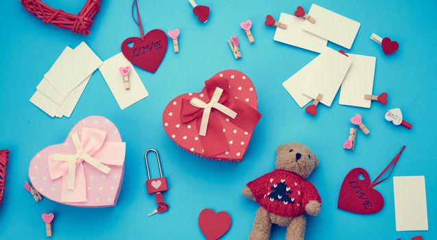 cardboard boxes in the form of a heart, a small teddy bear, white blank business cards with clothespins on a blue background, decor and objects for Valentine's Day, flat lay, copy space