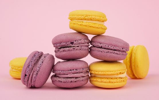 yellow in purple round baked macaroon cakes on a pink background, dessert stands in a stack, delicious