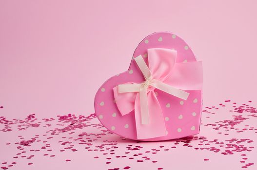 closed pink gift box in the form of a heart with a bow on a pink background, festive backdrop
