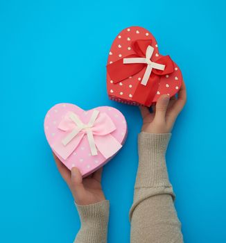 female hand holding a pink cardboard box with a bow on a blue background, concept of giving a gift for a holiday