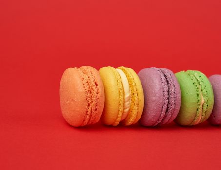 pile of multi-colored baked macarons almond flour cakes on a red background