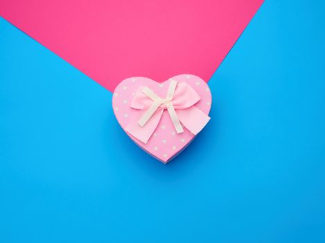 pink gift box in the form of a heart with a bow on a blue background, top view, festive backdrop