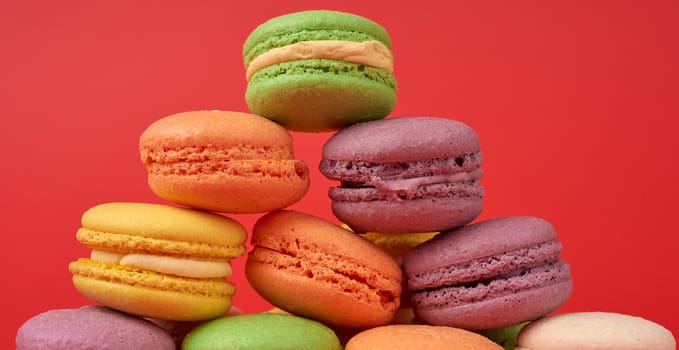 yellow, purple, green round baked macarons cakes on a red background, close up