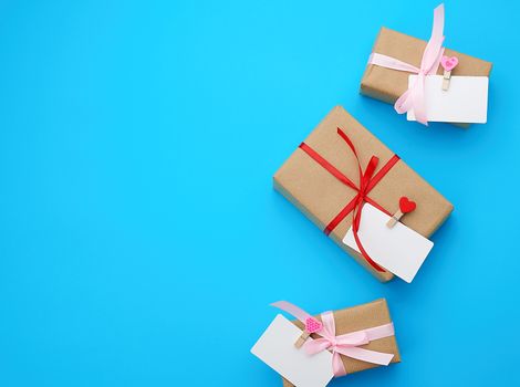 box is wrapped in brown paper and tied with a red thin silk ribbon on a blue background, copy space, holiday is Valentine's Day