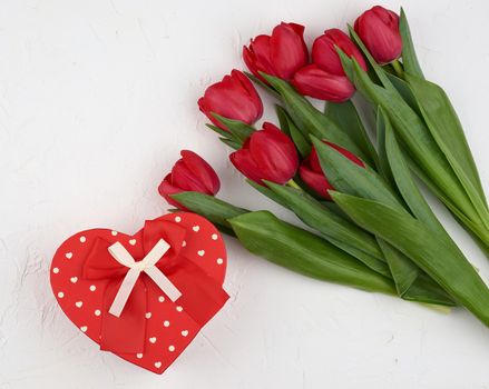 bouquet of red blooming tulips with green leaves, wrapped gift in brown craft paper on a white background, copy space. Festive backdrop for birthday, Valentine's day