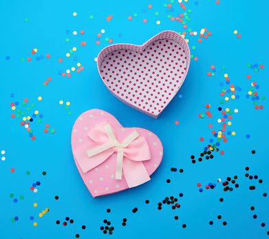 open pink heart-shaped cardboard box on a blue background with multi-colored shiny confetti, festive backdrop for birthday, Valentine's day