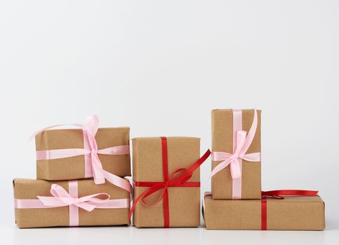 stack of gifts in boxes wrapped in brown kraft paper and tied with silk ribbon on a white background. Festive concept, copy space