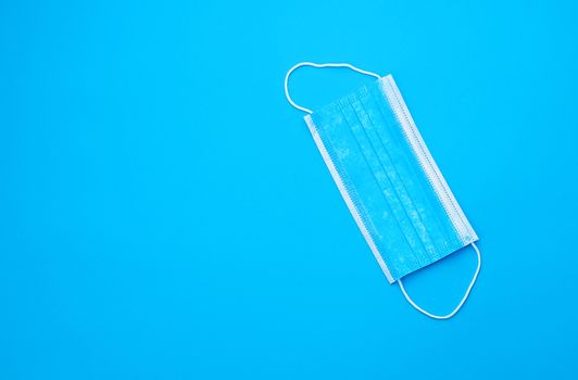 blue sterile medical mask with white elastic bands for doctors on a light blue background, flat lay, copy space